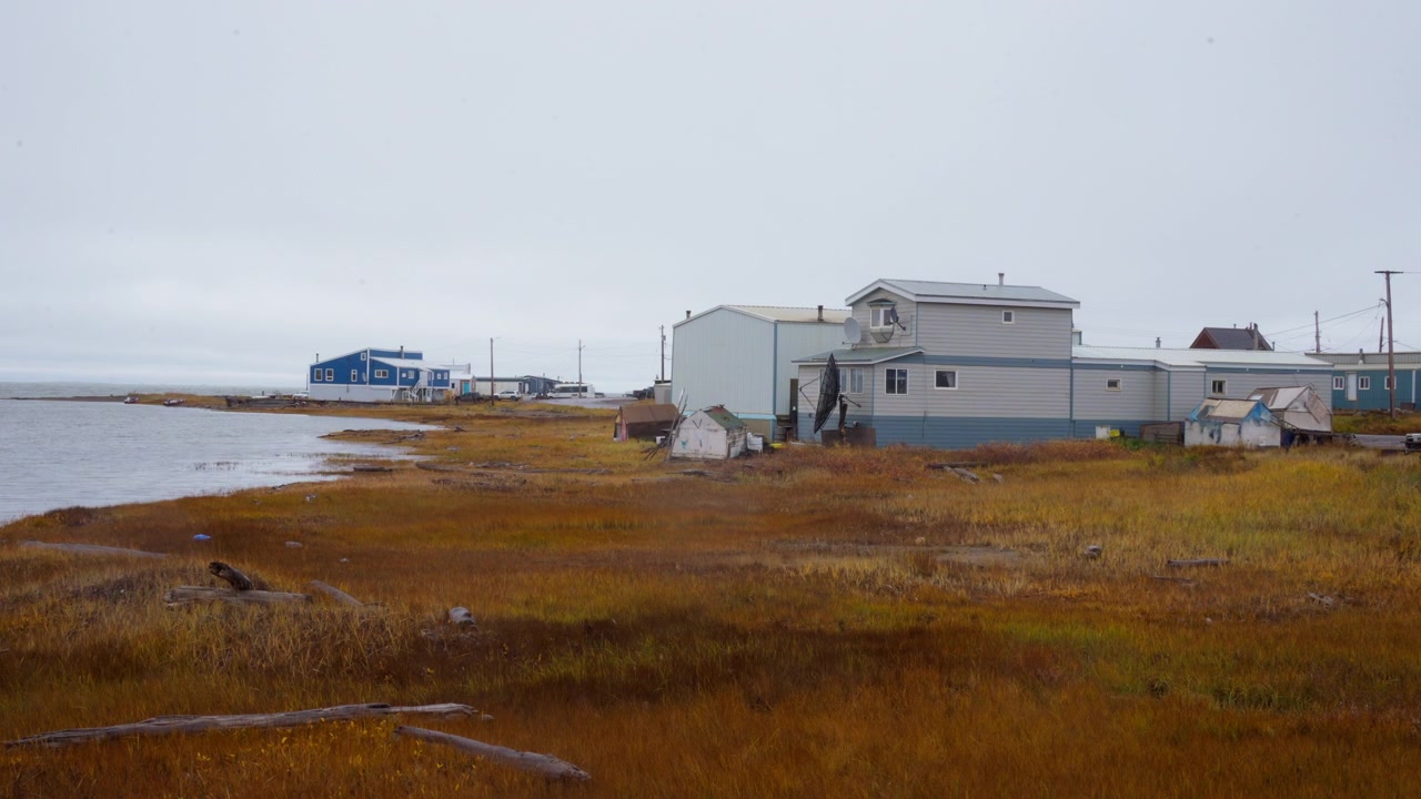 Tuktoyaktuk, NWT, Kanada – Bescheidene Gebäude und herbstliche Tundra säumen die ruhige Küstenlinie unter einem bedeckten Himmel – Statische Aufnahme.