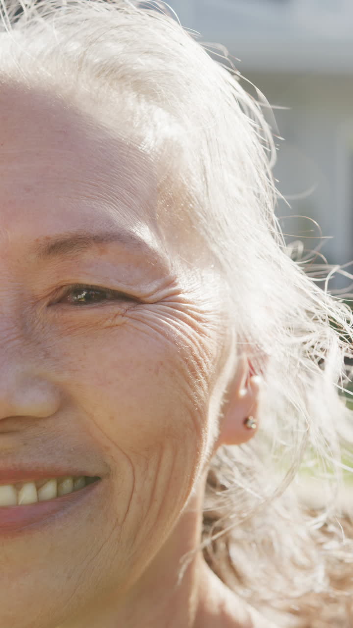 Vertical video of portrait of happy asian senior woman on sunny day in garden