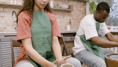 empleados con delantal verde modelando piezas de cerámica en torno de alfarero en un taller 1