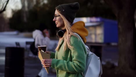 woman walking with hot drink and shack by winter city park