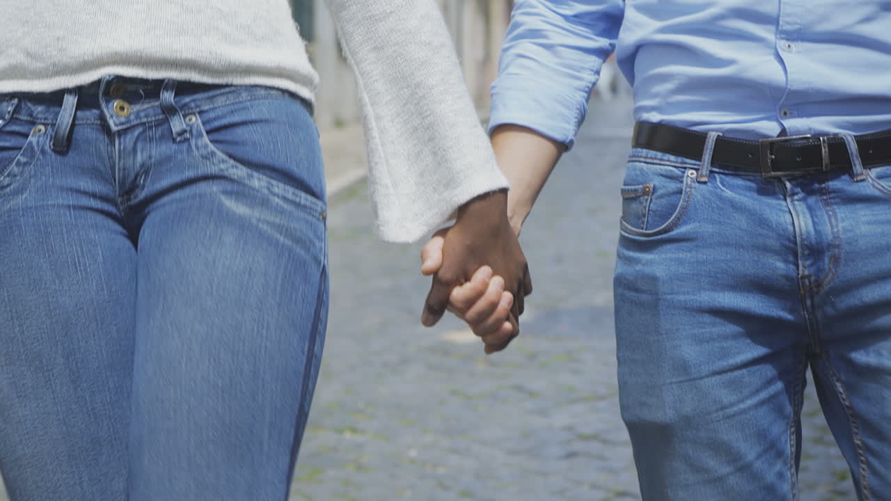 un primer plano de una pareja multirracial tomándose de las manos.