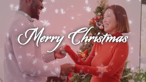 merry christmas text animation over couple exchanging gifts near christmas tree