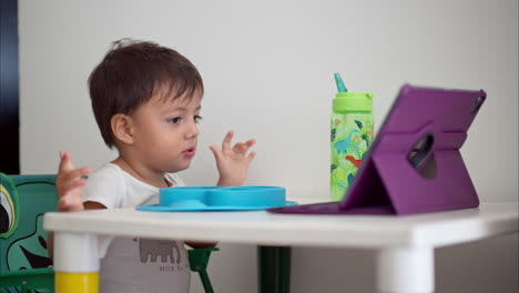 Cute-latin-boy-impressed-by-the-show-his-watching-on-a-purple-tablet-while-sitting-at-the-table