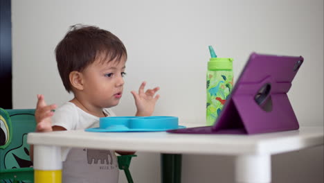 lindo chico latino impresionado por el programa que está viendo en una tableta morada mientras está sentado en la mesa