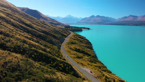 Picturesque-aerial-view-of-the-scenic-drive-along-turquoise-Lake-Pukaki-with-Mount-Cook-in-the-distance,-New-Zealand