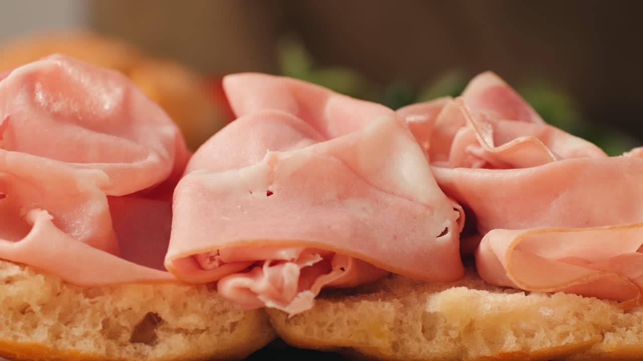 Mortadella ham sandwich, Traditional italian focaccia filled with thin pesto slices of mortadella, served by chef man in cafe restaurant. Macro of traditional italian spanish tapas antipasti.