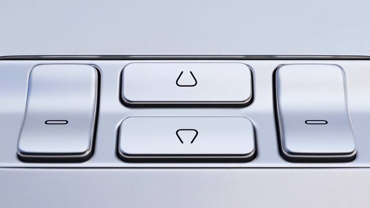 Light changes from amber to silver and blue over four raised buttons, revealing polished edges, dark gaps and simple black markings in tight symmetrical composition on metallic panel.