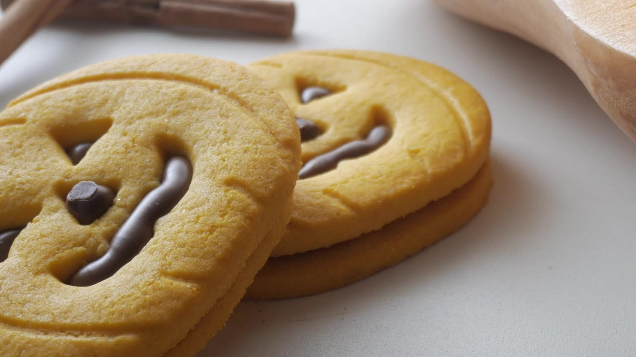 Close-up of jack-o'-lantern shaped cookies with chocolate details, resting on a white surface