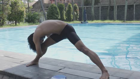 Un-Joven-Asiático-Estirando-Las-Piernas-Haciendo-Calentamiento-Junto-A-La-Piscina-Antes-De-Nadar-Por-La-Mañana.