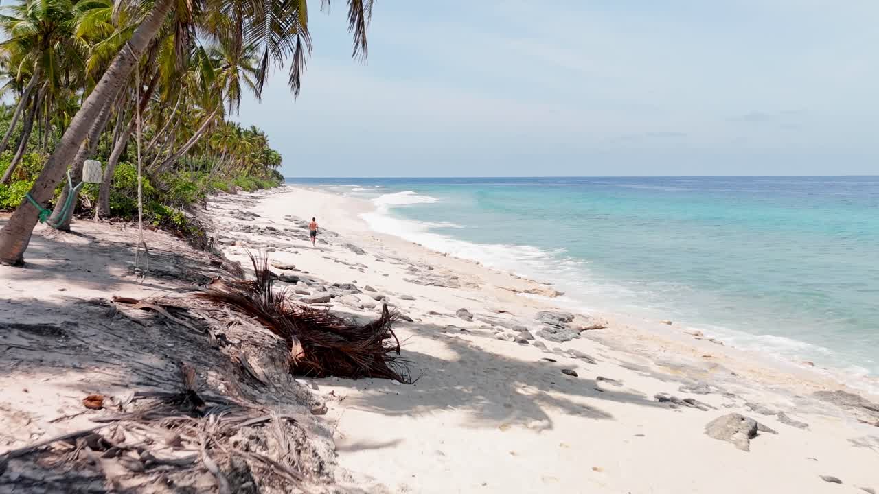 Dynamic aerial drone view of a man running along Geiymiskih Fannu Beach during sunset in Fuvahmulah, Maldives.
