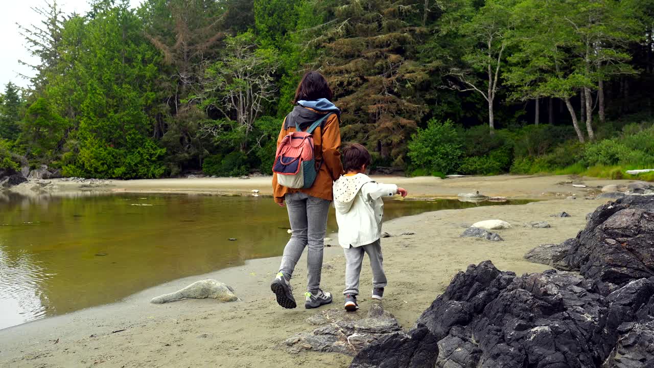 En mamma och ett barn som promenerar på en sandstrand vid en sjö