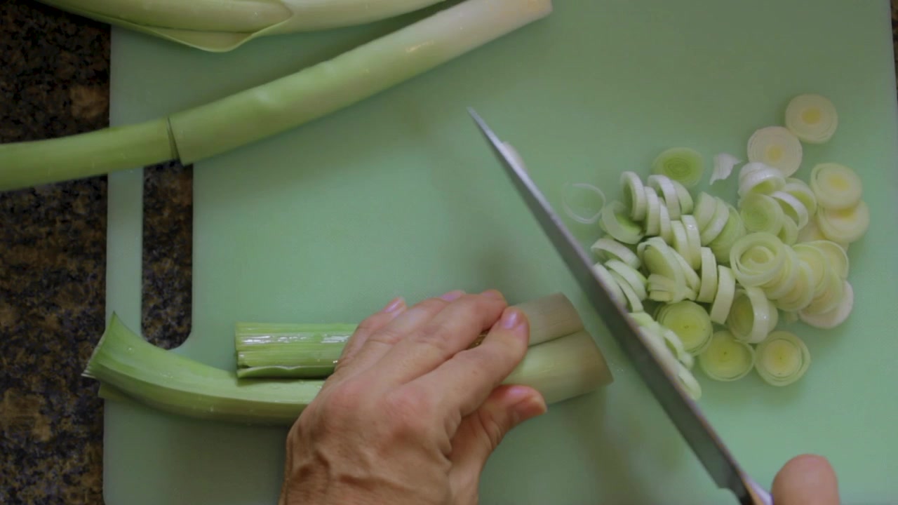 Woman cuts fresh leeks in a green plastic cutting board