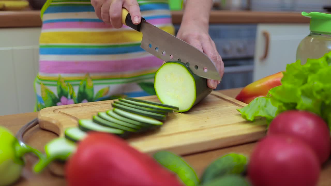 Women's hands Housewives cut with a knife fresh zucchini on the cutting Board of the kitchen table