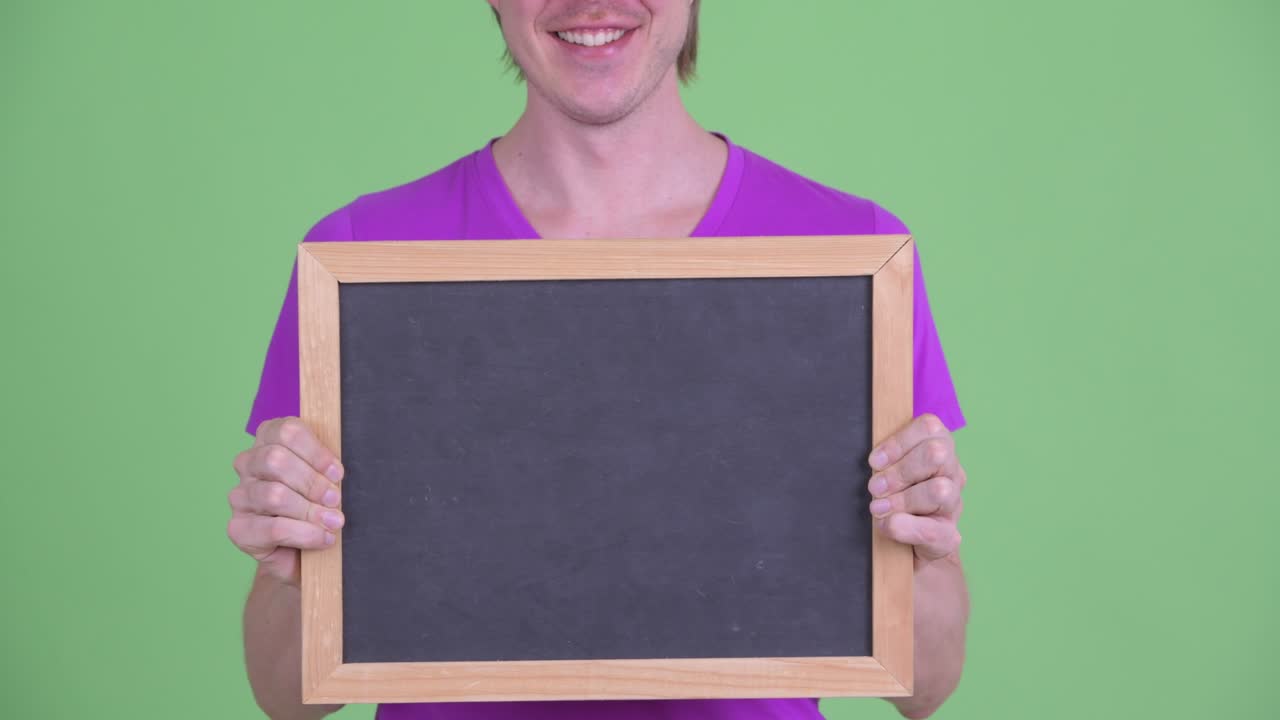 zoom en el tiro de un joven sonriendo y sosteniendo una pizarra con espacio de copia contra fondo verde