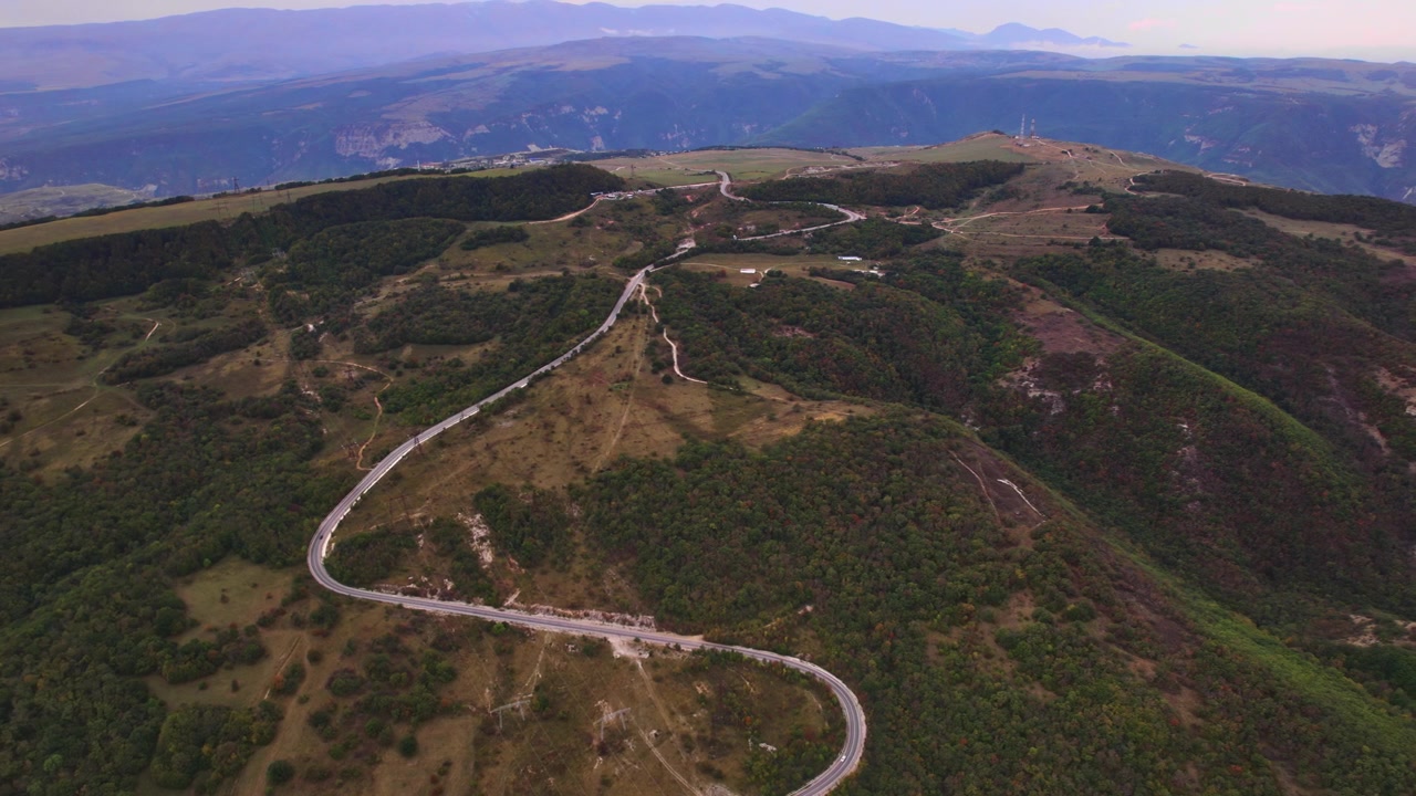 Una ripresa aerea cattura una strada tortuosa che attraversa una cresta verso un altopiano elevato, mentre una panoramica aerea sorveglia il percorso mostrando il design del tracciato, il terreno e lo scenario di viaggio remoto attraverso il Dagestan.