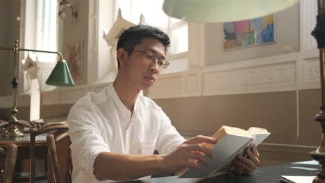 젊은 아시아 남성 학생이 도서관에서 책을 읽습니다.