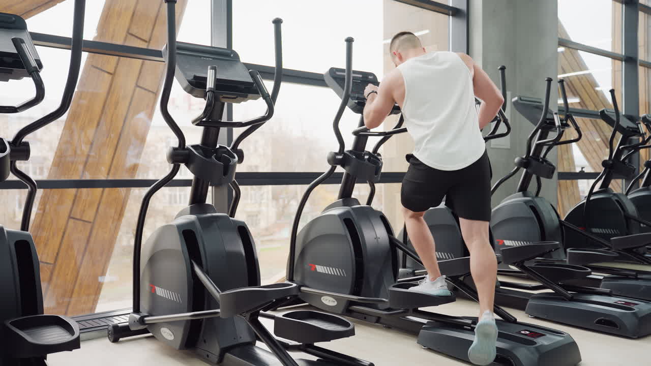 Gym instructor walks to exercise bikes steps on pedal adjusts digital console settings in bright modern gym next to mirror reflecting equipment and active posture ready for intense cardio session