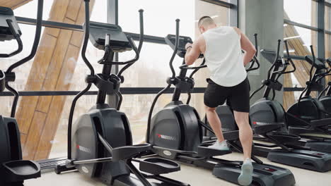 gym instructor walks to exercise bikes steps on pedal adjusts digital console settings in bright modern gym next to mirror reflecting equipment and active posture ready for intense cardio session