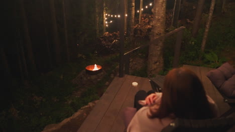 woman looks at campfire sitting on chair. young wife gets chance being alone with thoughts at campground. peacefulness of nature on terrace