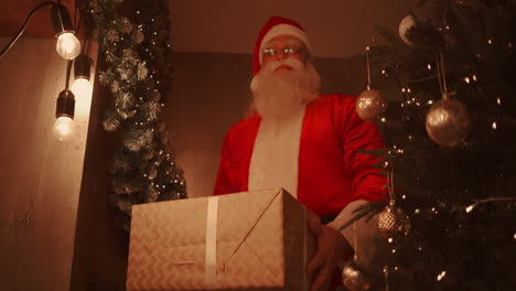 santa claus se inclina y pone una gran caja hermosa con un regalo para un buen niño bajo el árbol de navidad para el niño. imágenes de alta calidad 4k