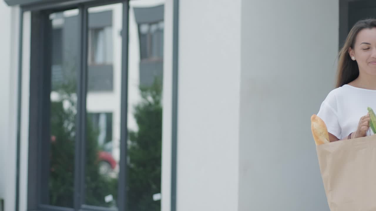 una mujer hermosa conoce a un repartidor que le da un paquete de compras con comida al lado de su casa. entrega de alimentos. concepto de mensajero, entrega a domicilio, compras en línea