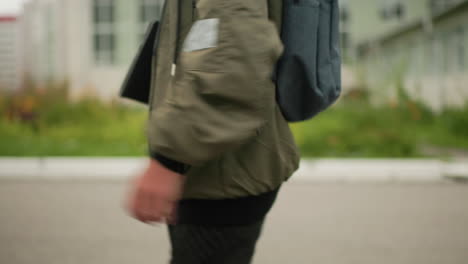 close up side view of young boy with backpack walking back home after school holding notepad under arm wearing jacket looking ahead with calm focused expression against brick wall background