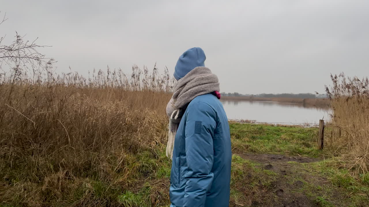 Slow motion track shot of young girl with blue jacket, scarf and hat walking along national park and smiling into camera