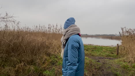 slow motion track shot of young girl with blue jacket, scarf and hat walking along national park and smiling into camera