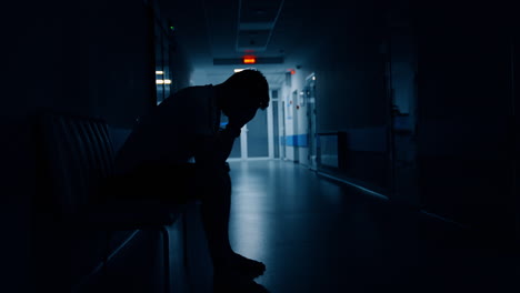 Man sitting in the dark corridor of the maternity hospital. Husband is worrying about wife giving birth to a baby.
