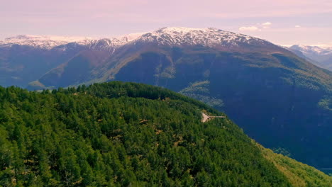 Snowy-mountain-peaks-and-woodland-area,-aerial-fly-forward-view