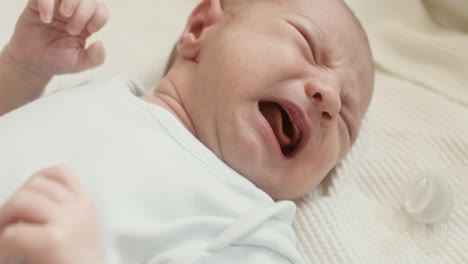 primer plano de un lindo bebé recién nacido acostado en la cama, llorando y luego calmándose