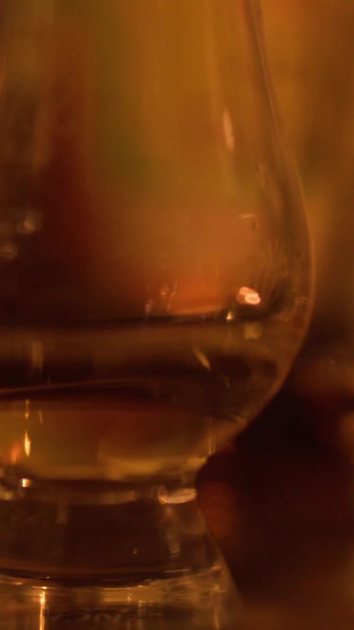 Primo piano di whisky ambrato che vortica in un bicchiere da degustazione sotto una luce calda e soffusa
