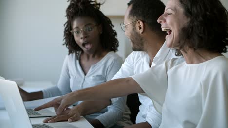 group of smiling workers talking and pointing at laptop