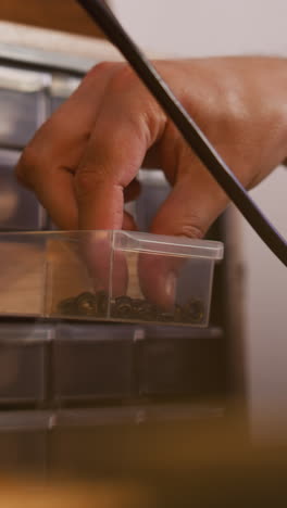 employee chooses metal rivet in small plastic drawer in manufacturing workshop closeup. fastening tool usage in studio. repaired supplies storage