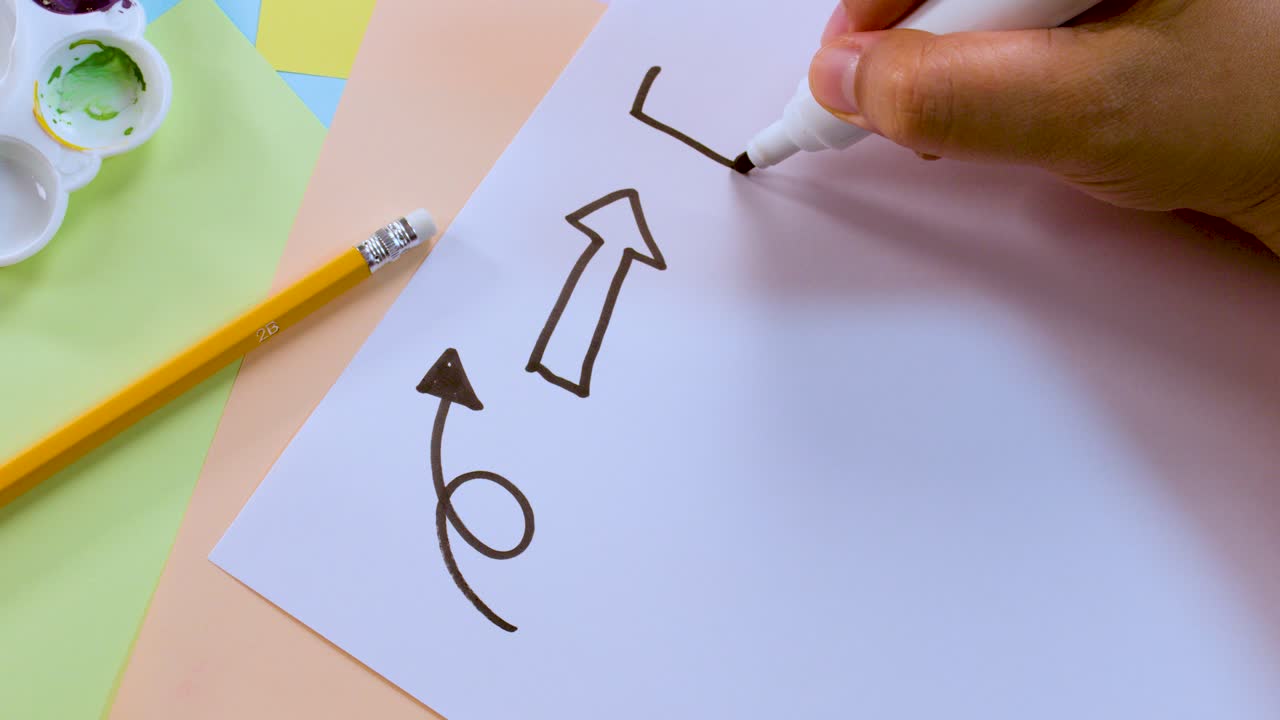 Una persona disegna frecce in grassetto e volute con un pennarello su carta, vista dall'alto, illuminazione intensa