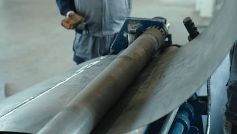 passing a sheet of metal through a round shaft. metal rolling machine working in industrial workshop