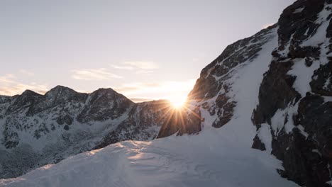 lateral panning reveals a glowing sunrise cresting the mountain summit in a tranquil high-altitude setting.