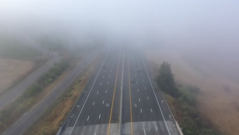 aerial view of traffic headed over a bridge into thick fog on major freeway