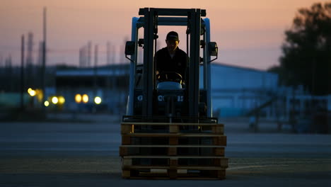 a worker driving a forklift with pallets at twilight