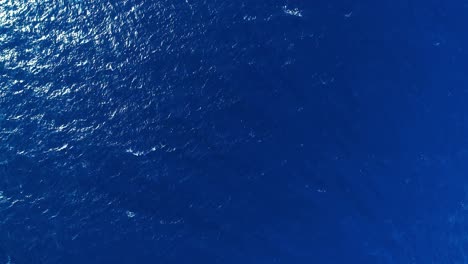 Panoramic-wide-angle-top-down-of-clean-blue-ocean-wave-texture-with-sun-rays-on-bottom-right-corner
