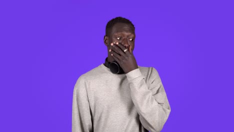 portrait of handsome young man in white shirt and headphones on neck - super shocked and surprised with eyes and mouth wide open, touching face, isolated on blue background. human emotions