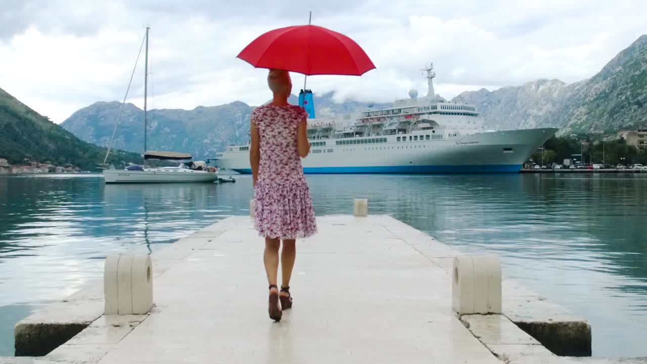 женщина, идущая по пирсу с зонтиком, с видом на круизный корабль и море