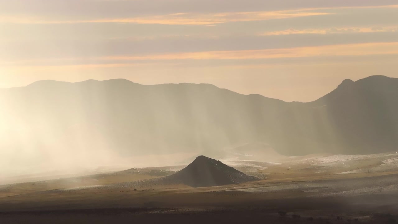 Vue aérienne par drone d'une pluie rare tombant sur le désert du Namib, créant un contraste saisissant entre des nuages sombres, du sable mouillé et de vastes paysages désertiques