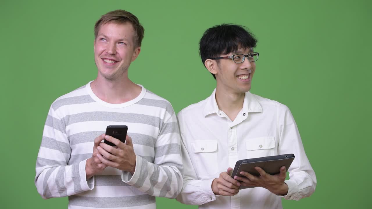 두 명의 행복한 젊은 다민족 사업가들이 소셜 미디어 개념을 위해 전화와 디지털 태블릿을 사용합니다.