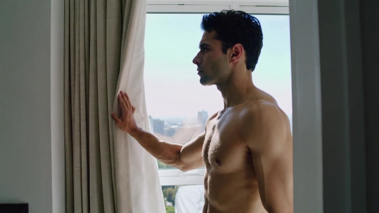 Tirando la tenda, un uomo a torso nudo si affaccia alla finestra, appoggiando una mano, osservando lo skyline in cerca di un riflesso.