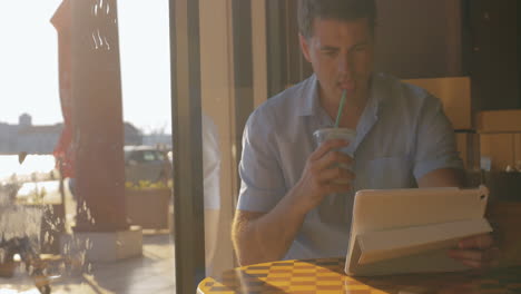 Un-Joven-Buscando-Algo-En-Una-Tableta-Bebiendo-Té-Helado-Del-Túbulo.