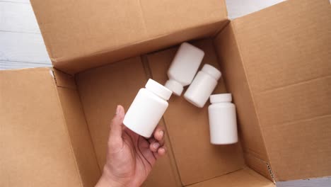 hand holding white medicine bottles inside an open cardboard box.