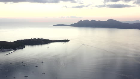 AERIAL:-Ocean-with-Sailboats-and-Tropical-Island-with-Mountains-in-Background-at-Sunrise-Vacation,-Travel,-Sunset