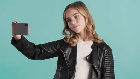 una adolescente caucásica con chaqueta de cuero tomando selfies con su teléfono inteligente.