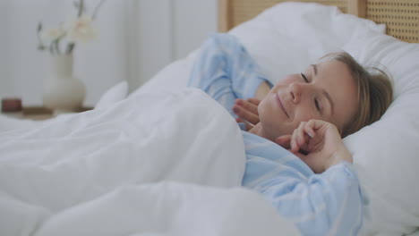 Pretty-young-smiled-Caucasian-woman-waking-up-in-the-morning-and-stretching-in-her-bed-and-looking-content.-Indoors